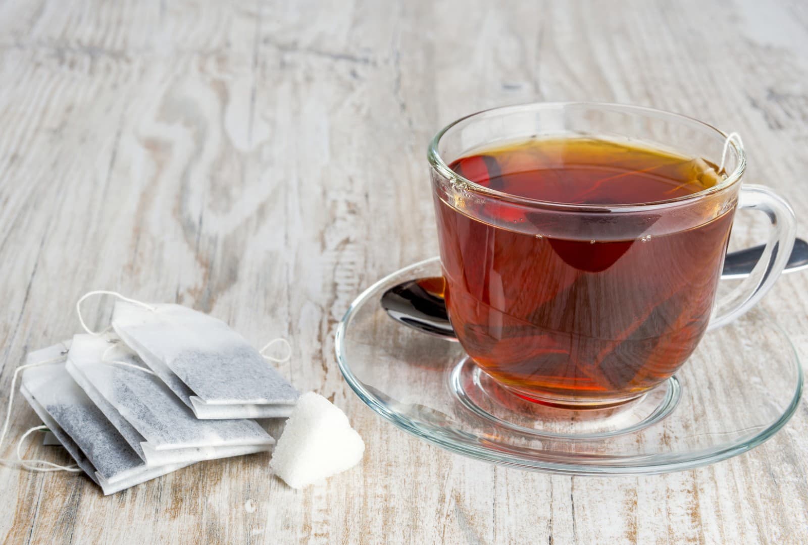 Tea bags beside a glass cup of black tea and a sugar cube